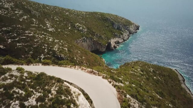 4K Aerial footage of a car driving along winding coastal road at Zakynthos island, Greece.
