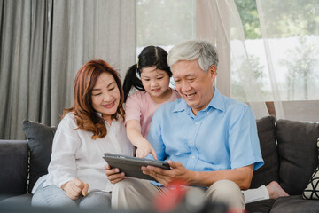 Asian grandparents and granddaughter using tablet at home. Senior Chinese, grandpa and grandma...