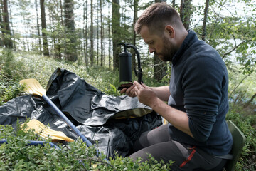 Concentrated, serious man holds a pump in hands for pumping a rubber boat, there are oars nearby,...