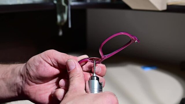 An optician technician polishes the frame of glasses. A professional optician fixes glasses.