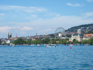 Boat trip on Lake Lucerne. View from the boat to the houses on the lake shore. There are some boats sailing on the lake and a Ferris wheel is in the background