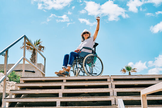 Happy woman in wheelchair waving hand on street