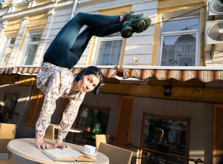 Woman doing handstand on the cafe table with coffee and read a book in cafe outdoor. Concept of...