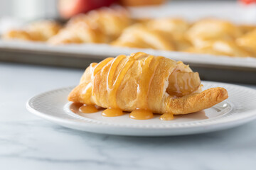 Close up front view of a freshly baked apple filled crescent roll drizzled with caramel sauce.