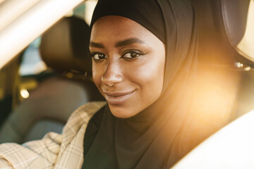 Black woman wearing headscarf smiling while driving car