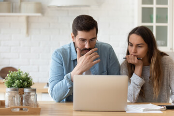 Serious concerned married couple sit indoor looking at laptop read news, receive notification from bank about overspend, financial debt, feel worried, learn new conditions, high rates, taxes concept