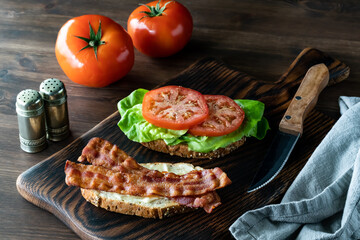 Open faced bacon and tomato sandwich on a wooden board, ready for eating.