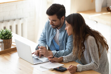 Busy serious couple sit in kitchen look at laptop screen calculate expenses paying through e-bank...