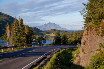 The asphalt road goes beyond the turn opening a wonderful view of the Norwegian landscape with mountains, forests, rocks and fjords. Norway.