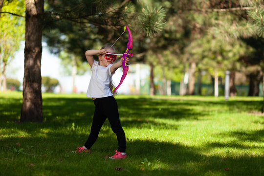 Child Girl Playing Archer In The Park At Leisure. An Active Hobby Outdoors.