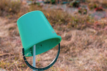 A garden plastic empty bucket hangs overturned on a peg in the garden. Narrow focus.