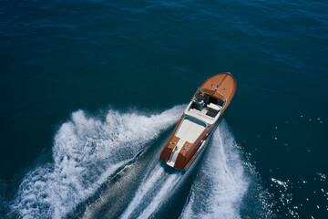 Classic Italian wooden boat fast moving aerial view. Top view of a wooden powerful motor boat. Luxurious wooden boat fast movement on dark water. - obrazy, fototapety, plakaty