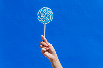 Crop woman with sweet lollipop on blue background