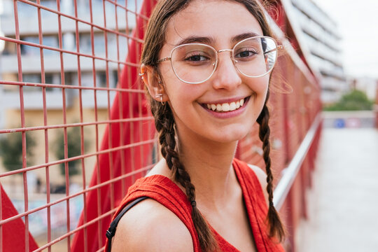 Happy woman in glasses and with pigtails looking at camera in city