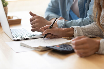 Close up spouses calculating family budget paying utility bills online using laptop, check loan...