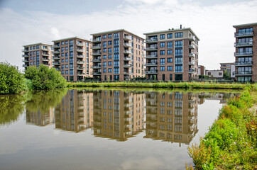 Oegstgeest, The Netherlands, July 11, 2021: Modern residential buildings with brick facades reflecting in a small lake on a sunny day in summer