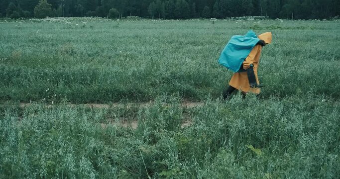 Man engaged in hiking in a yellow raincoat carries a woman with a backpack in a blue raincoat through a field. The concept of getting injured during a hike and mutual assistance in extreme conditions