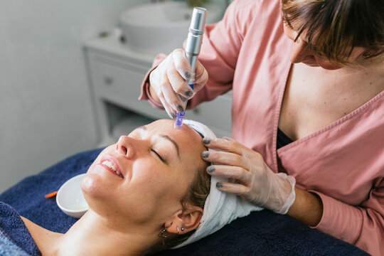 Crop cosmetologist doing microdermabrasion procedure of face of client