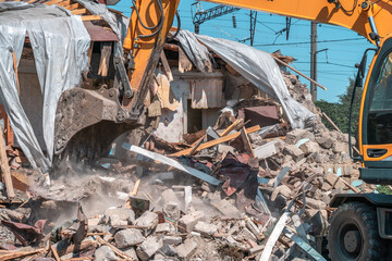 Hydraulic excavator bucket breaks walls of building. Demolition of dilapidated housing.