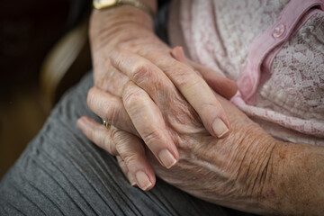 Close horizontal view on the folded wrinkled hands of an old senior woman, 80s adult, grandmother, praying. Selective focus.