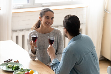 Above view husband makes a toast to wife during family holiday celebration, people sit in modern kitchen holding glasses of red wine enjoy romantic date. Congratulations, wishes, life events concept