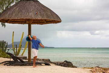 Happy caucasian boy plays on one of the best Mauritius beach on rainy cloudy day, catches ball to...