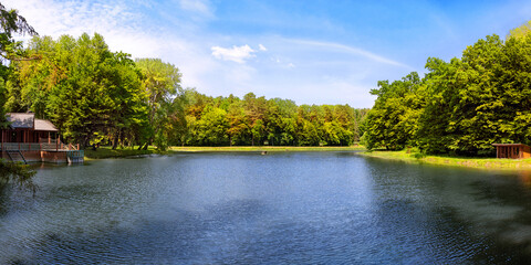 Panoramic view on lake in forest with lush green trees, blue sky and sunlight in sunny summer day, National Botanical Reserve of Vorotniv, Ukraine.