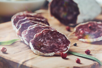 Sliced french salami with fresh rosemary and on rustic wooden background. Close up. 
