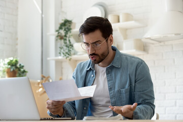 Man sit at table in domestic kitchen reading bad news in received correspondence paper letter feels...