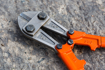 A bolt cutter with metal hands painted orange on a concrete slab background