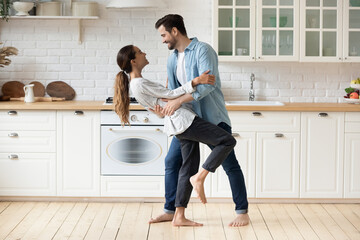 Young beautiful mixed race couple home owners family celebrate relocation day housewarming dancing in modern cozy kitchen standing barefoot on warm floor feel happy. Romance, dating, bank loan concept