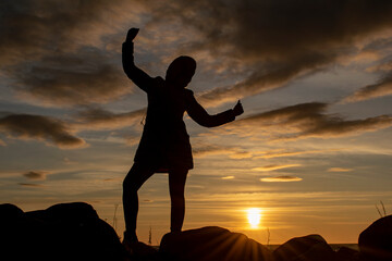 Fototapeta premium Silhouette of a young girl with a triumphantly thrown up hand against the background of the evening sky. World perception concept.