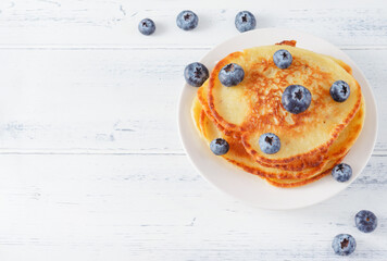 pancakes with blueberries on a plate on a light wooden table