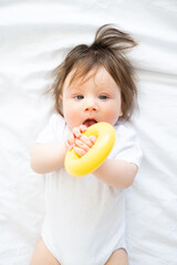 cute baby boy lying on bed and play with yellow plastic circle toy.