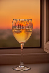 A glass of white wine on the windowsill against the background of the sunset.