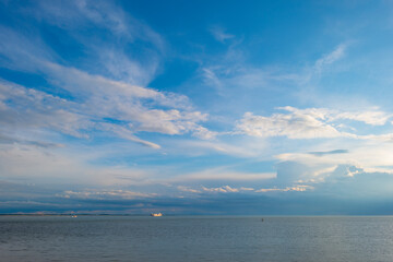 Obraz premium Sea along a coast under dark white clouds in a blue sky illuminated by the light of a colorful sundown sun in summer, Vlissingen, Walcheren, Zeeland, the Netherlands, July, 2021
