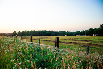 evening view of the farm, summer sunset, beautiful wood fence, haystacks and a mowed field of grass