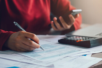 Close up woman using a pen filling form of Individual Income Tax Return, in living room at...