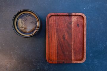 Black coffee cup and blank wooden pad. Dark mug of espresso or Americano on concrete table...