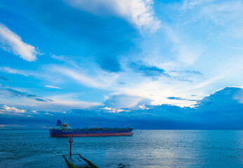 Naklejka premium Sea along a coast under dark white clouds in a blue sky illuminated by the light of a colorful sundown sun in summer, Vlissingen, Walcheren, Zeeland, the Netherlands, July, 2021