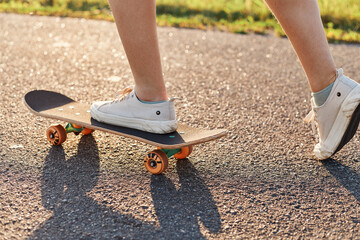 Faceless female skateboarding outdoor on asphalt road in summertime, spending time in active way,...