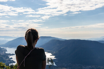 A woman standing at the viewing platform of a church at the top of Oswaldiberg with the view on the Lake Ossiacher in Austrian Alps. A bit of overcast. The woman enjoys panoramic view. Freedom