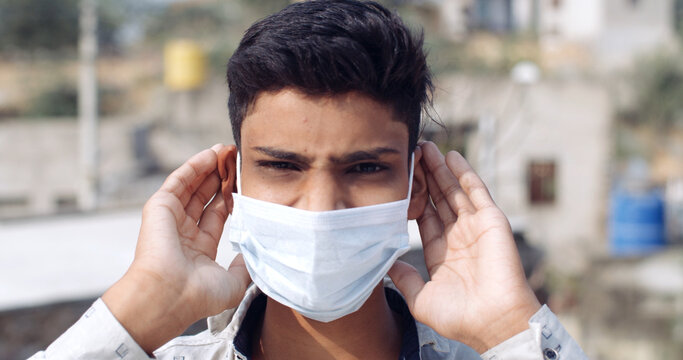 Closeup of a young Indian boy wearing a Covid mask and touching his ears with a frowny face