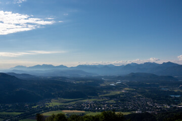 Naklejka premium A panoramic view on the valley at the foothill of Austrian Alps. The mountains in the back are very steep and sharp. Lush pastures in front. Clear and blue sky. Serenity and calmness.