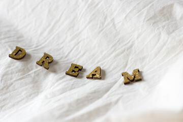 golden glitter wooden letters on a fabric background arranged to form the word dream - photographed...