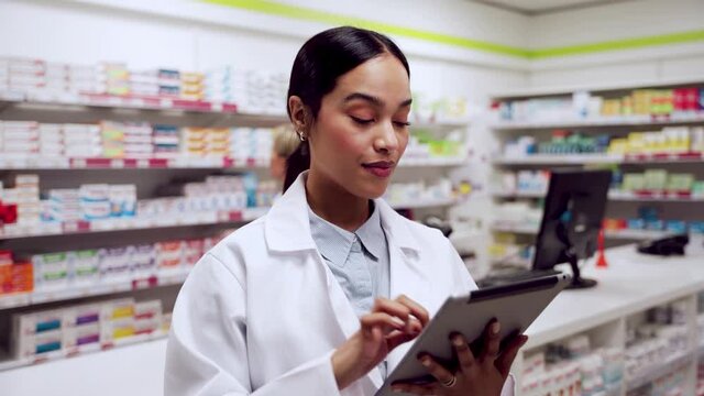 Mixed race female pharmacist working in pharmacy typing on digital tablet