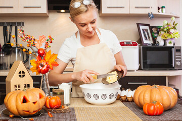 A woman puts butter in the cookie dough for Halloween in the kitchen with autumn decor.