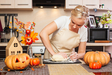A woman kneads cookie dough for Halloween in the kitchen with autumn decor.