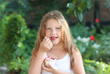 Tanned beautiful healthy girl with long hair with granola, yogurt and berry smoothie dessert in her hands. Child has a healthy and delicious breakfast dessert