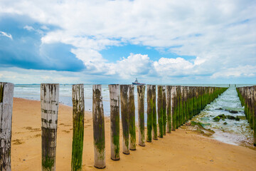 Sunlit waves on the yellow sand of a sunny beach along the North Sea illuminated by the light of a colorful sun and a blue cloudy sky in summer, Walcheren, Zeeland, the Netherlands, July, 2021
